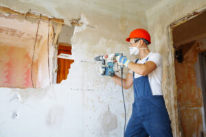 Worker wearing protective equipment drilling into a wall during demolition where asbestos testing may be required