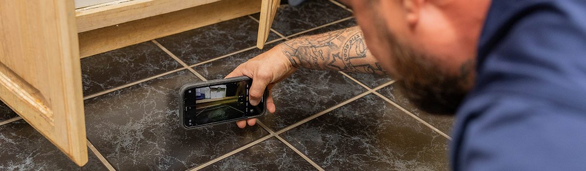 Technician documenting hidden damage during mold removal by inspecting beneath cabinetry in a residential home
