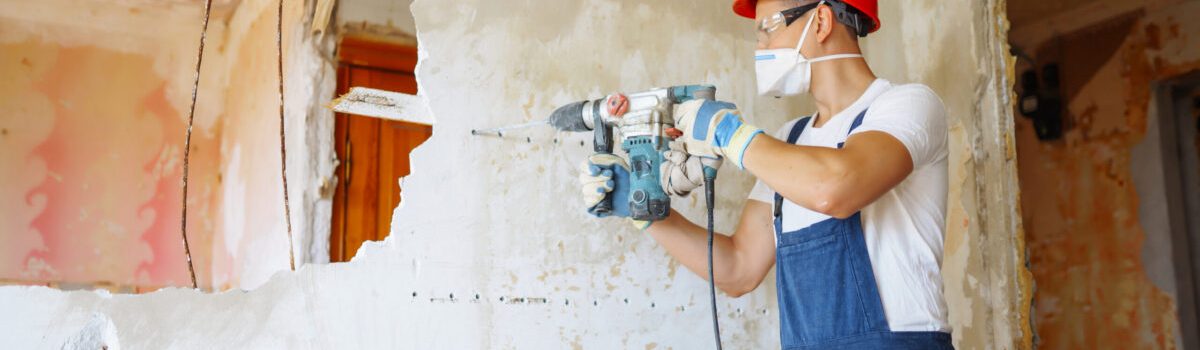 Worker wearing protective equipment drilling into a wall during demolition where asbestos testing may be required